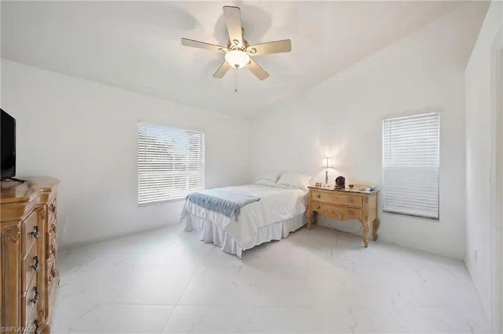 Bedroom featuring an angled ceiling with a ceiling fan, two windows with blinds, and white tile flooring