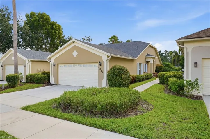 Stucco exterior featuring an attached garage with a sectional door, concrete driveway, and a walkway leading to the entry