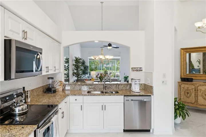 Kitchen featuring white cabinetry, granite countertops, stainless steel appliances, and an arched pass-through opening