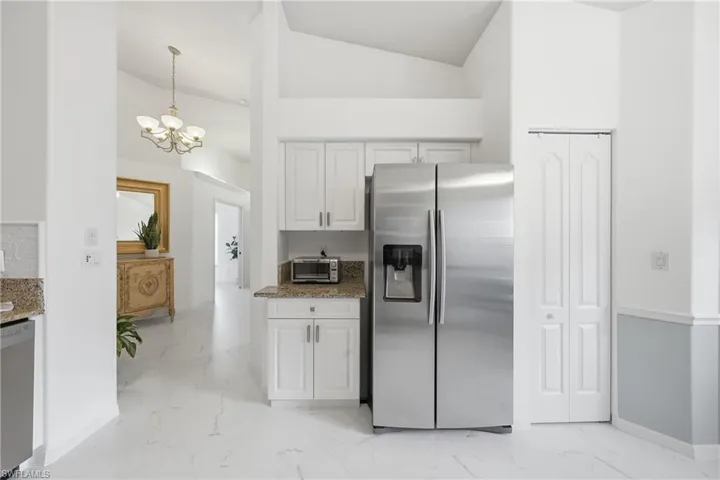 Kitchen area featuring stainless steel French door refrigerator, white cabinetry, and granite countertops