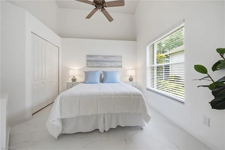 Vaulted ceiling bedroom featuring a ceiling fan, white bi-fold closet doors, a large window with blinds, and light-toned tile flooring