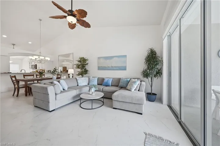 Vaulted ceiling great room featuring white tile flooring, a paddle-blade ceiling fan, and sliding glass doors