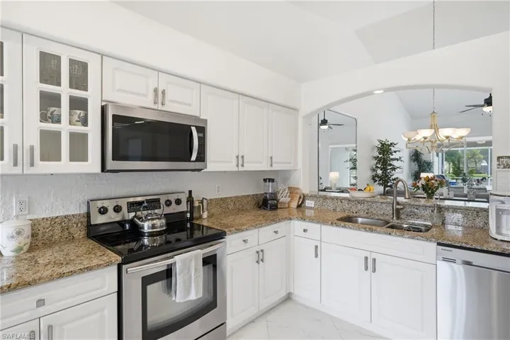 Kitchen featuring white cabinetry, granite countertops, stainless steel appliances, and a pass-through window with an arched opening