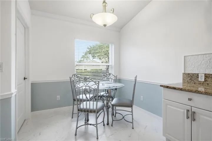 Dining area featuring vaulted ceilings, light-hued walls with wainscoting, white tile flooring, and a window with blinds