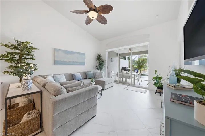 Living area featuring vaulted ceilings, large format tile flooring, and sliding glass doors opening to an outdoor screened patio