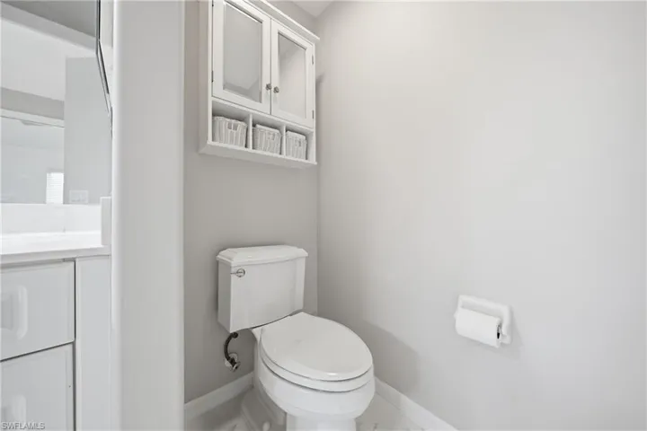 Bathroom featuring a white toilet, wall-mounted storage cabinet with glass-front doors, and a vanity with a white countertop and flat-panel cabinetry
