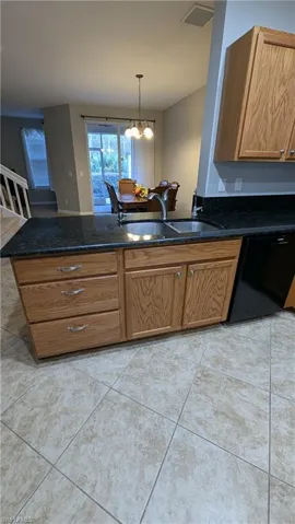 Kitchen with brown cabinetry, dishwasher, pendant lighting, a peninsula, and dark stone counters