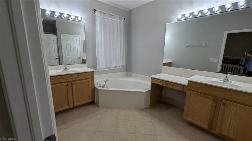Bathroom with two vanities, a bath, and light tile patterned floors