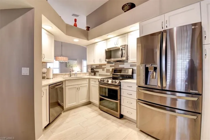 Kitchen with appliances with stainless steel finishes, decorative backsplash, pendant lighting, and white cabinetry
