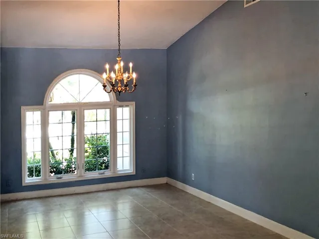 Bright dining room with chandelier, vaulted ceiling, and tile flooring