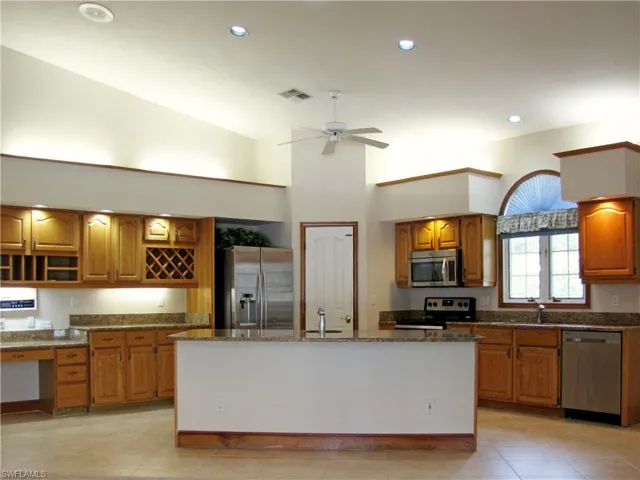 Kitchen with steel finishes, oak cabinetry, stone countertops, and an island with sink
