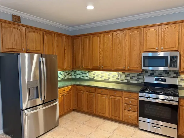 Kitchen featuring stainless steel appliances, ornamental molding, brown cabinets, and decorative backsplash