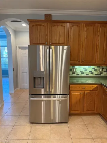 Kitchen with arched walkways, crown molding, stainless steel fridge with ice dispenser, light tile patterned floors, and brown cabinetry