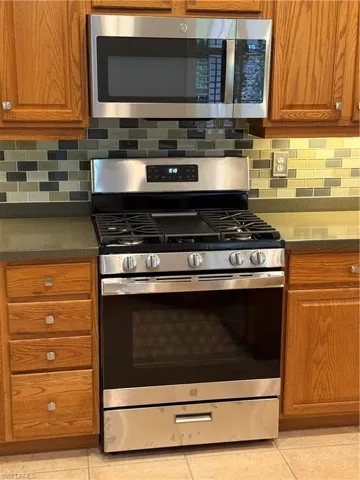 Kitchen featuring stainless steel gas range, backsplash, and brown cabinetry