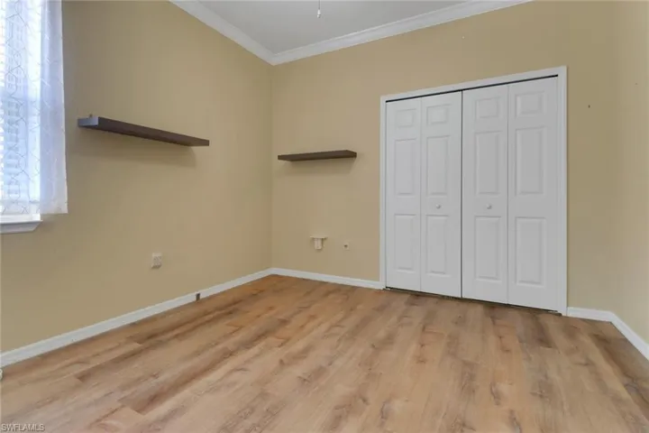 Unfurnished bedroom with a closet, baseboards, crown molding, and light wood-type flooring
