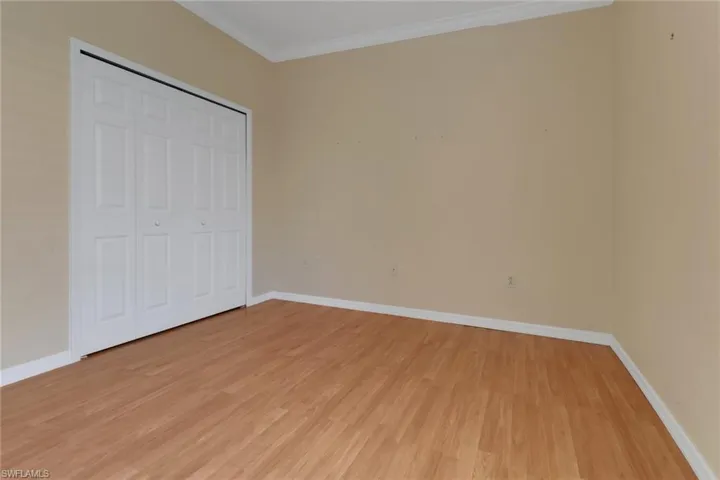 Unfurnished bedroom with a closet, baseboards, ornamental molding, and light wood-style flooring