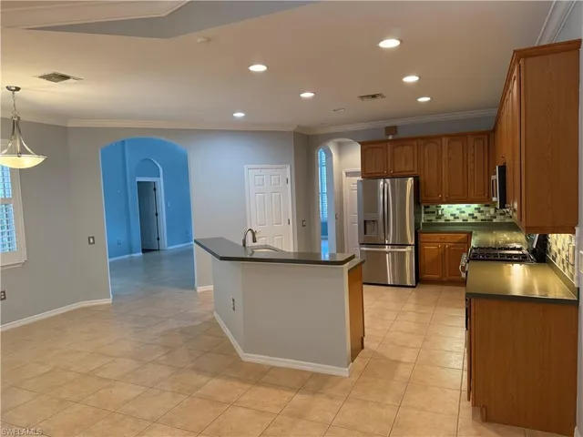 Kitchen with dark countertops, ornamental molding, appliances with stainless steel finishes, arched walkways, and brown cabinetry
