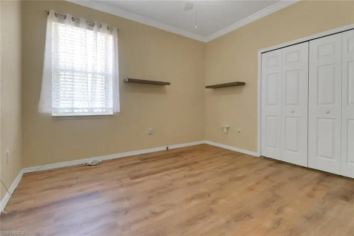 Unfurnished bedroom featuring baseboards, wood finished floors, ornamental molding, and multiple windows