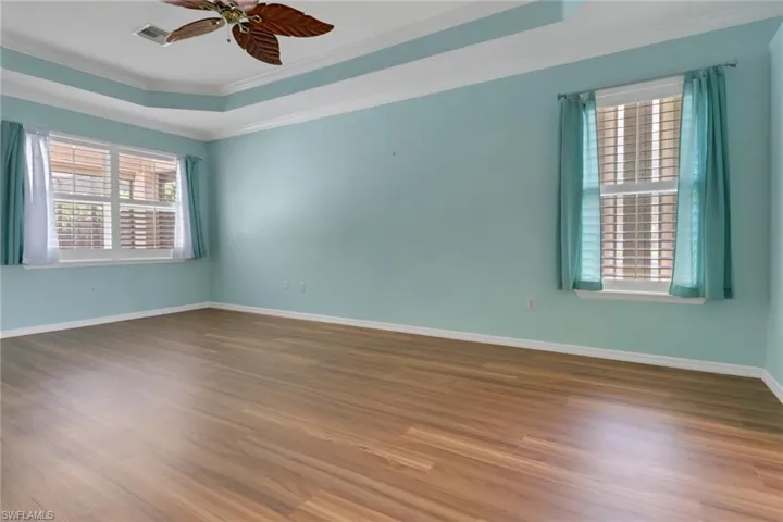 Unfurnished room with wood finished floors, ceiling fan, a raised ceiling, ornamental molding, and visible vents