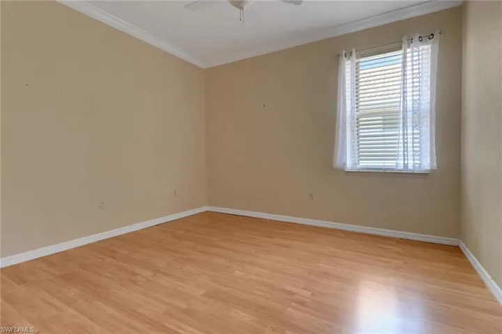 Empty room featuring light wood-style flooring, crown molding, baseboards, and a ceiling fan