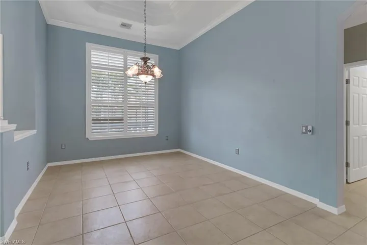 Unfurnished room featuring a tray ceiling, ornamental molding, light tile patterned floors, baseboards, and a notable chandelier