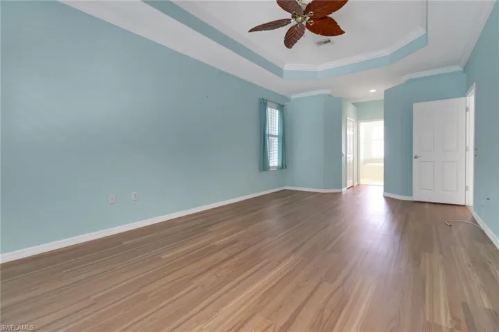 Empty room featuring a tray ceiling, wood finished floors, crown molding, baseboards, and ceiling fan