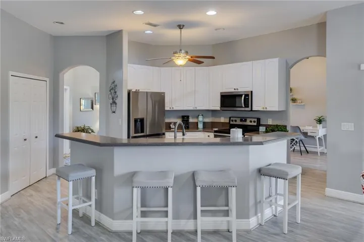 Kitchen featuring white cabinetry, stainless steel appliances, an integrated breakfast bar, wood-finish flooring, and recessed lighting