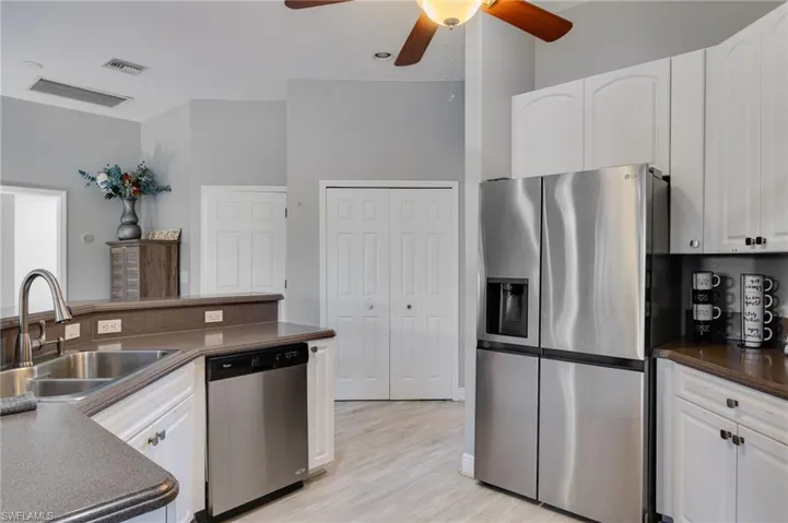 Kitchen featuring white cabinetry, stainless steel appliances, a double basin sink with a high-arc faucet, and wood-finish flooring