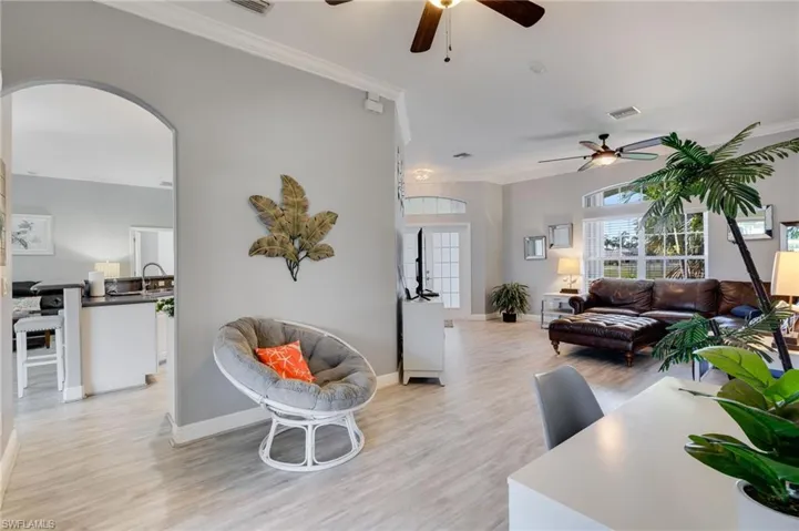 Open-concept living space featuring light wood-finish flooring, an arched doorway, crown molding, and ceiling fans