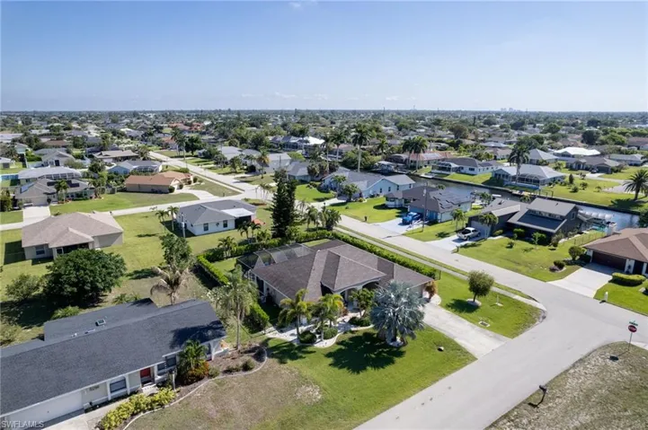 Residential neighborhood featuring a canal, mature trees, paved streets, and single-story homes with various rooflines