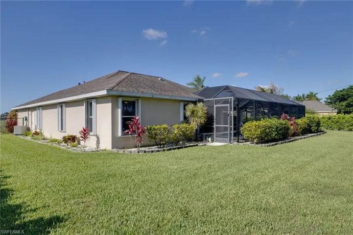 Expansive lawn area featuring a stucco exterior, a screened enclosure, mature landscaping, and a well-defined planting bed border