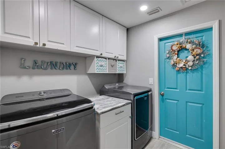 Laundry area featuring white shaker-style cabinetry, a built-in countertop, a top-load washing machine, a front-load dryer, and a vibrant turquoise paneled door