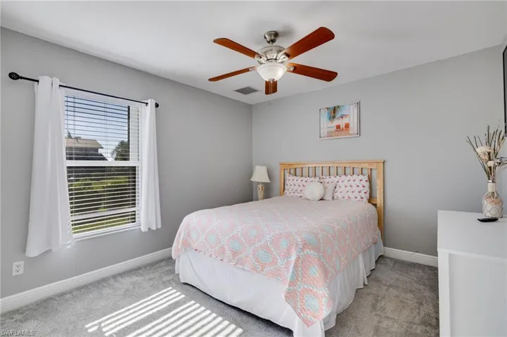 Bedroom featuring light gray wall paint, gray carpeting, a window with blinds and white curtains, a ceiling fan with light, and white baseboards