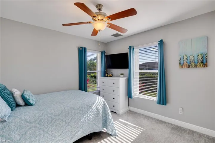 Bedroom featuring a ceiling fan with integrated lighting, two windows with blinds and blue curtains, light grey wall paint, and grey carpet flooring