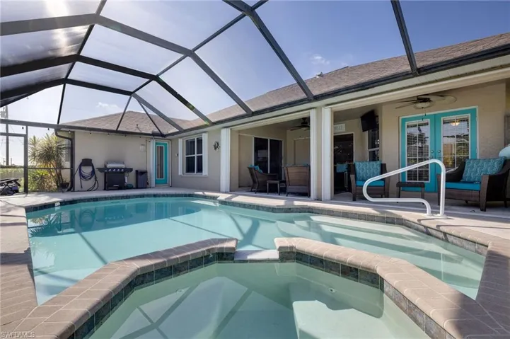 Screen-enclosed pool area featuring a rectangular pool with integrated spa, a paved deck, an exterior patio with ceiling fans, and direct access to the interior via double glass doors
