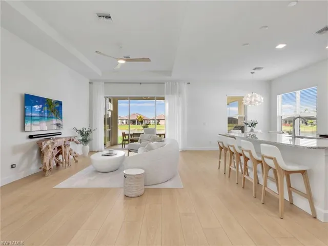 Living room with a ceiling fan, light wood-style flooring, a raised ceiling, a chandelier, and recessed lighting