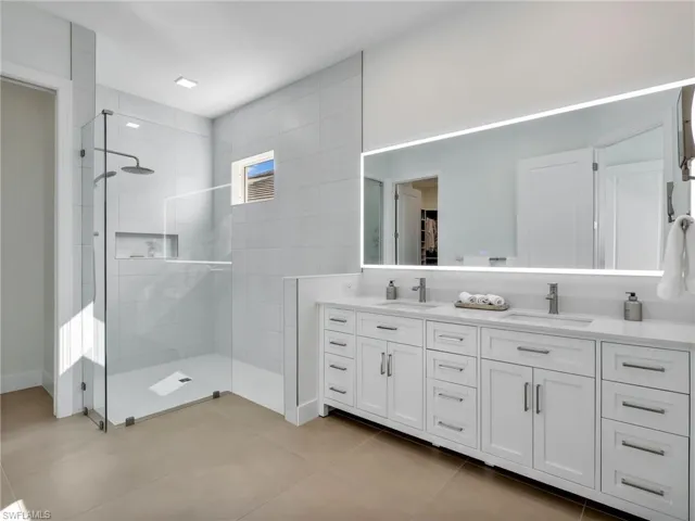 Bathroom with double vanity, a shower stall, light tile patterned flooring, and a spacious closet