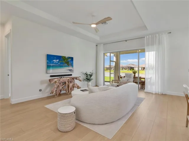 Living area featuring a tray ceiling, a ceiling fan, light wood-style flooring, and a residential view