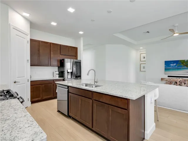 Kitchen featuring open floor plan, light stone counters, light wood-style flooring, an island with sink, and recessed lighting