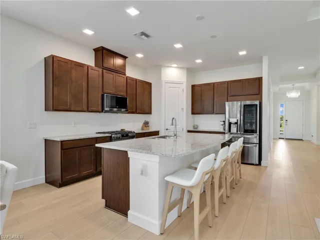 Kitchen with dark brown cabinetry, a kitchen breakfast bar, stainless steel appliances, light wood finished floors, and light stone countertops