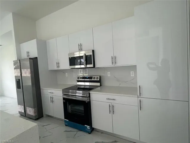 Kitchen featuring appliances with stainless steel finishes, white cabinetry, tasteful backsplash, and light tile flooring