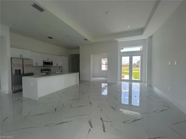 Kitchen featuring light tile floors, a center island, sink, white cabinets, and appliances with stainless steel finishes