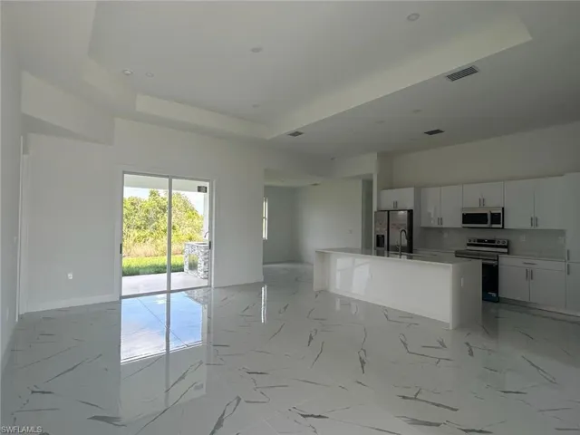 Kitchen featuring white cabinetry, stainless steel appliances, a tray ceiling, a kitchen island with sink, and light tile floors