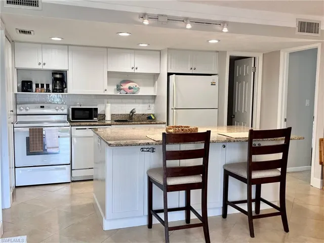 Kitchen with white appliances, white cabinetry, light stone counters, open shelves, and recessed lighting