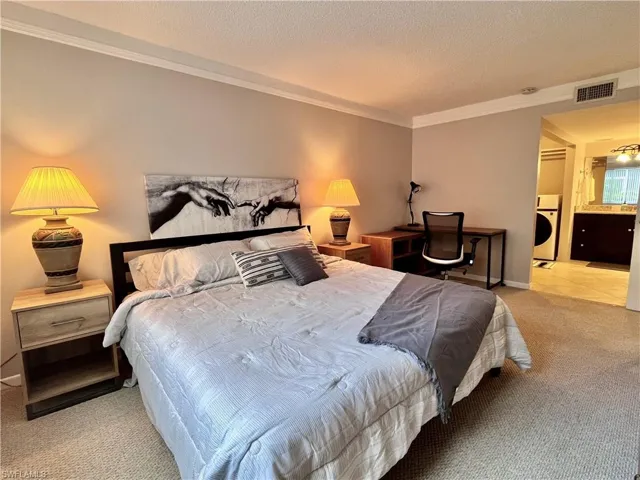 Primary Bedroom with light colored berber carpet, crown ornamental molding, office desk and large walk in closet including washer/dryer combination unit, and ensuite bath with shower.