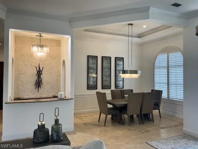 Dining area featuring light tile patterned floors, ornamental molding, a raised ceiling, and a chandelier