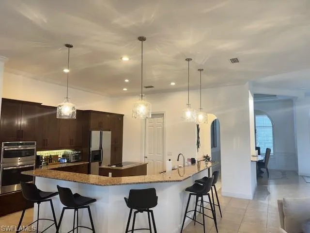 Kitchen featuring stainless steel appliances, a large island, decorative light fixtures, and dark brown cabinets