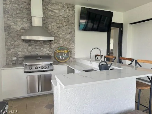 Kitchen featuring light tile patterned flooring, sink, a breakfast bar area, kitchen peninsula, and wall chimney range hood