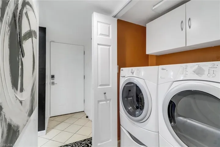 Clothes washing area featuring cabinets, washer and clothes dryer, and light tile patterned flooring