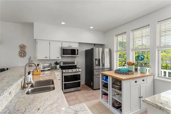 Kitchen featuring white cabinetry, open shelves, stainless steel appliances, light stone countertops, and recessed lighting